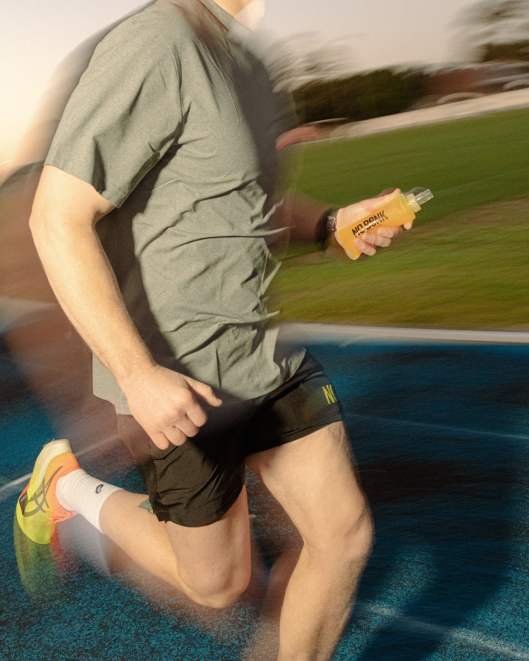 A runner mid-stride on a blue track, panned, carrying a filled NOBONK soft flask