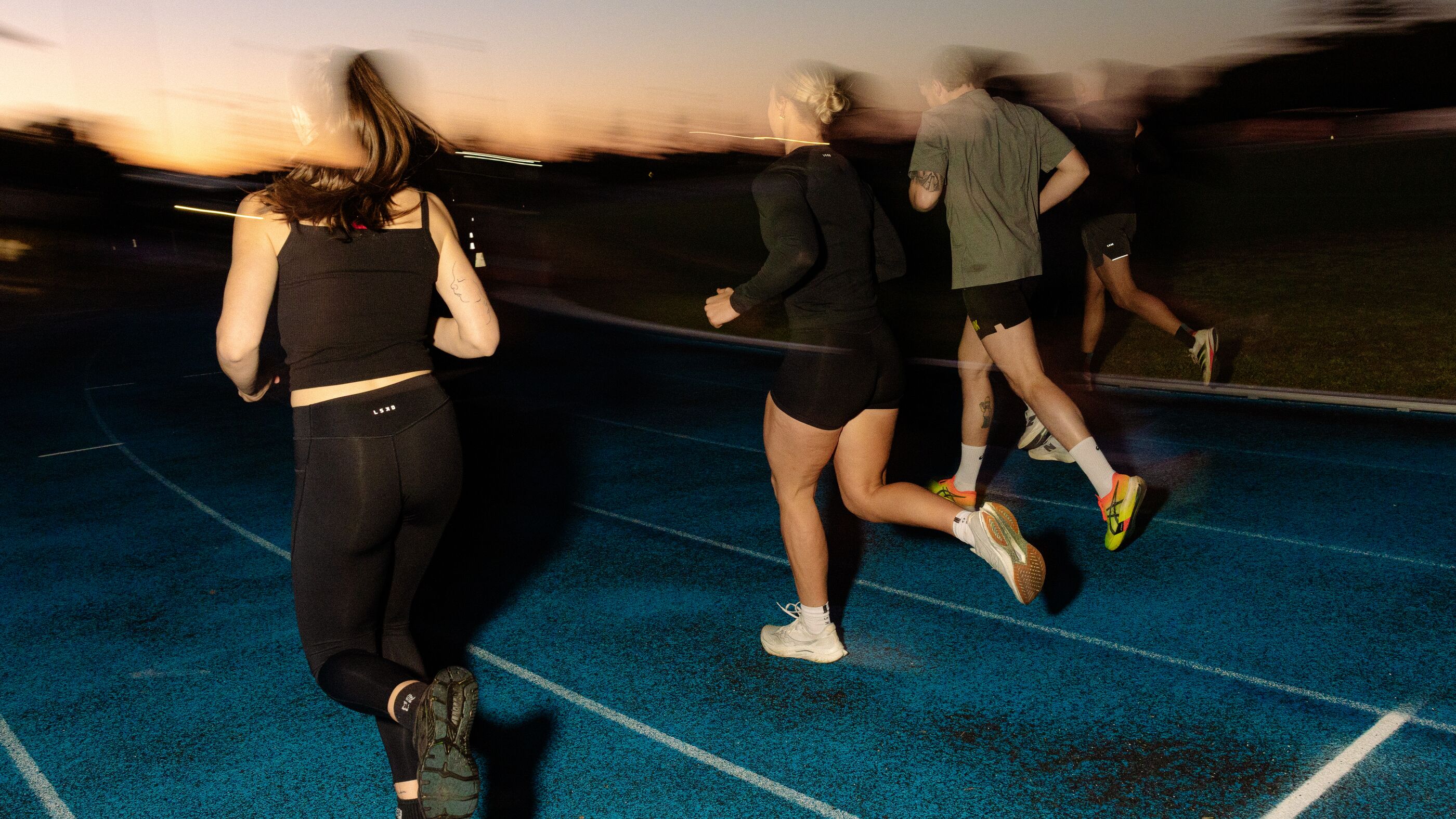 A group of runners heading away down a blue track as the sun comes up behind the treeline