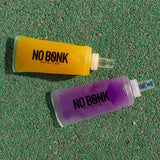 A filled NOBONK soft flask and a Grape flask lying on a green track surface