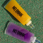 Two NOBONK soft flasks, Pineapple Mango and Grape, on a green track surface