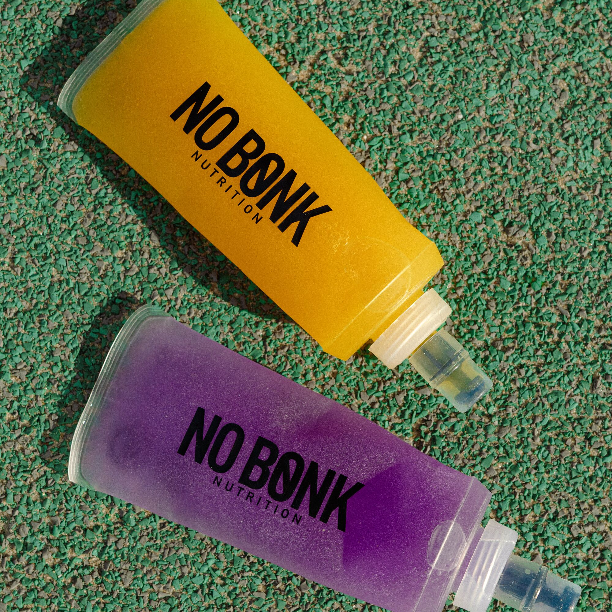 Two NOBONK soft flasks, Pineapple Mango and Grape, on a green track surface