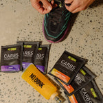 Six NOBONK sachets fanned out on concrete beside a running shoe and a filled flask