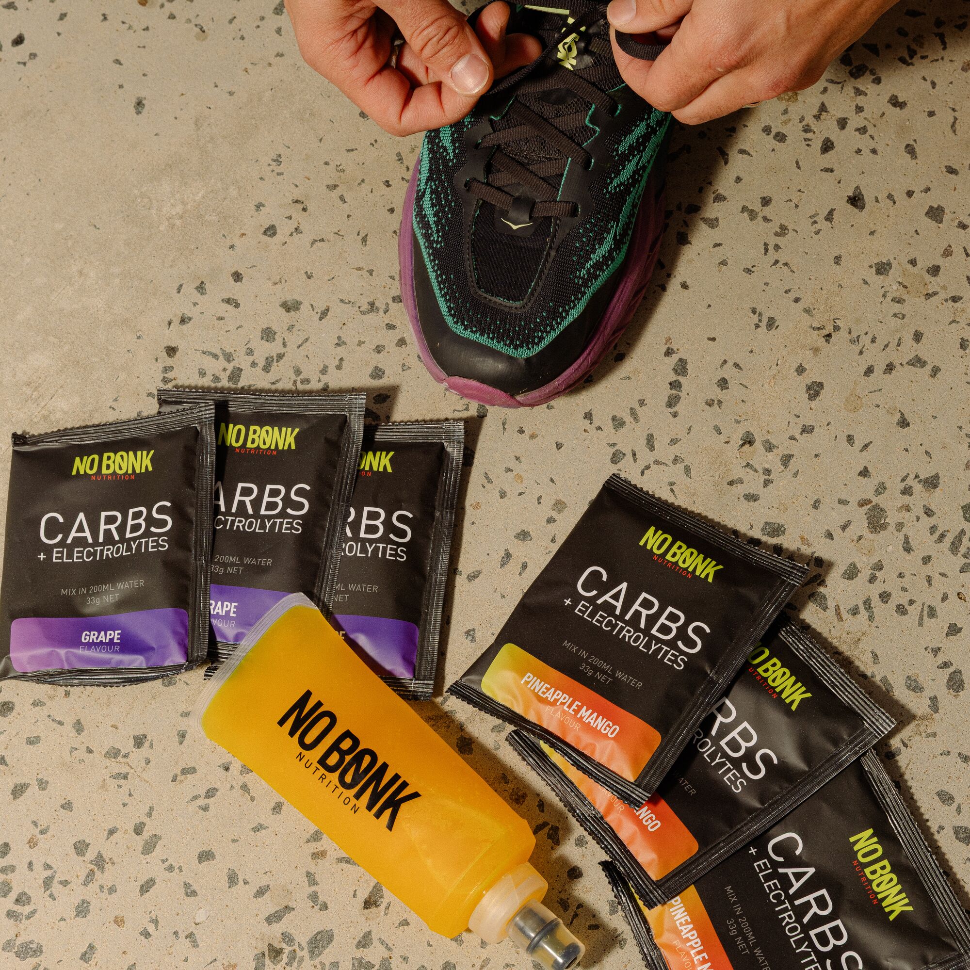 Six NOBONK sachets fanned out on concrete beside a running shoe and a filled flask