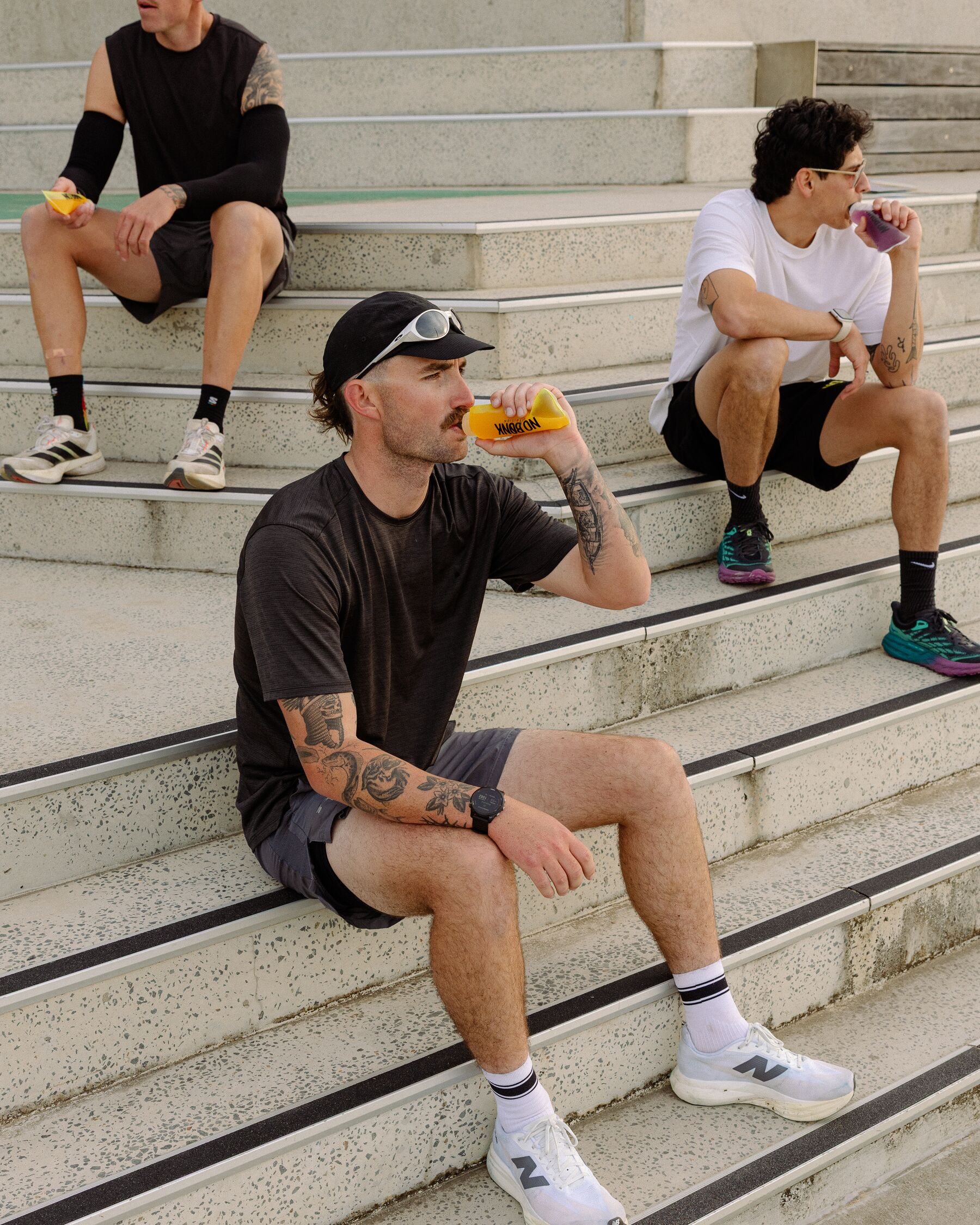 Three runners resting on concrete steps, drinking NOBONK from soft flasks