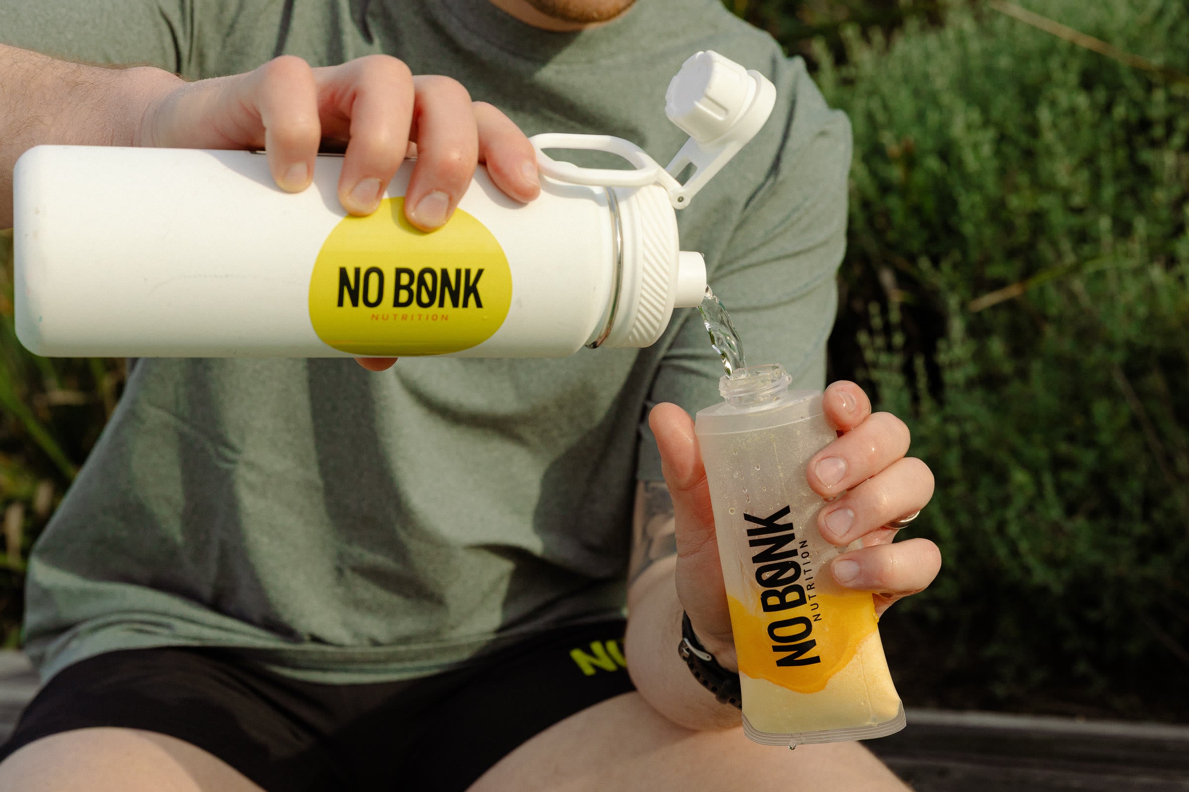 Water being poured from a NOBONK bidon into a soft flask holding a Pineapple Mango serve